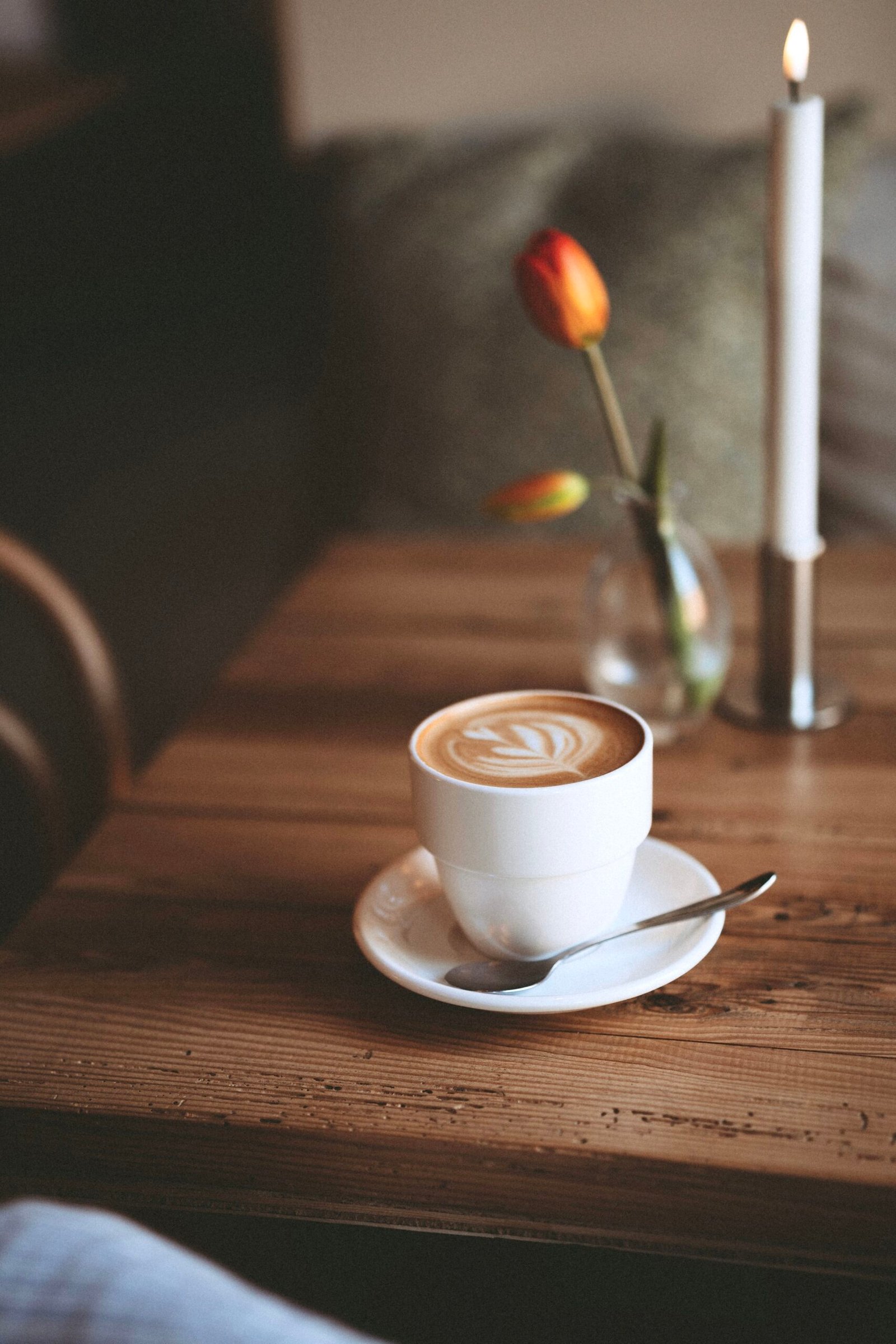 Cappuccino på et træbord ved siden af en tulipan og stearinlys